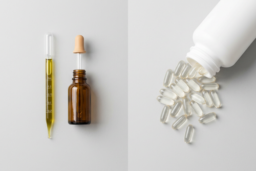 A marked 1 mL pipette of golden oil and an amber glass dropper bottle on the left, a pile of large white softgel capsules spilling from a plastic bottle on the right.